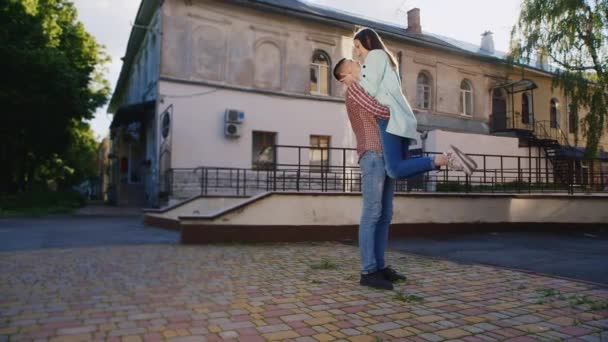 Молодая пара обнимается на улице, парень держит девушку на руках. Они целуются.
. - Кадры, видео