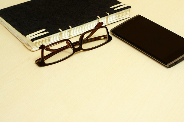 Γυαλιά, μαύρο σημειωματάριο και smartphone σε φόντο ξύλινη. - Φωτογραφία, εικόνα