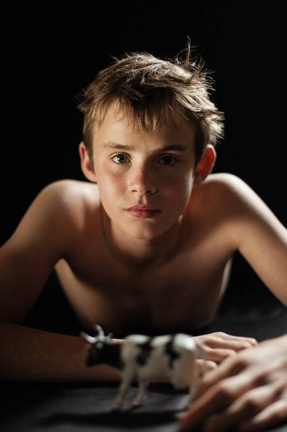 Shirtloser Teenie-Junge liegt mit Spielzeugkuh auf Bauch - Foto, Bild