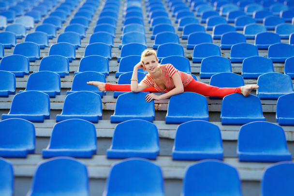 Sporty woman doing the splits on stadium's seats - Foto, afbeelding