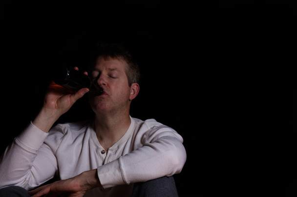 Depressed mature man drinking a beer in dark background - Фото, зображення