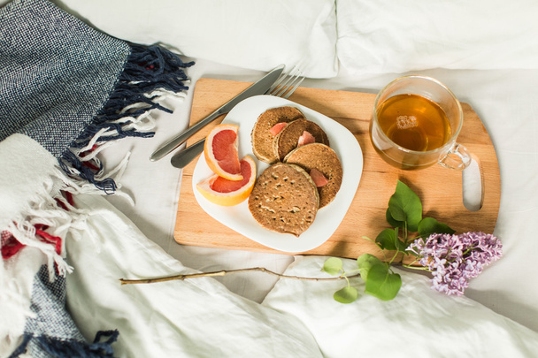 Breakfast in bed, Oatmeal pancakes with grapefruit and tea. Branch of lilac - Foto, Imagen