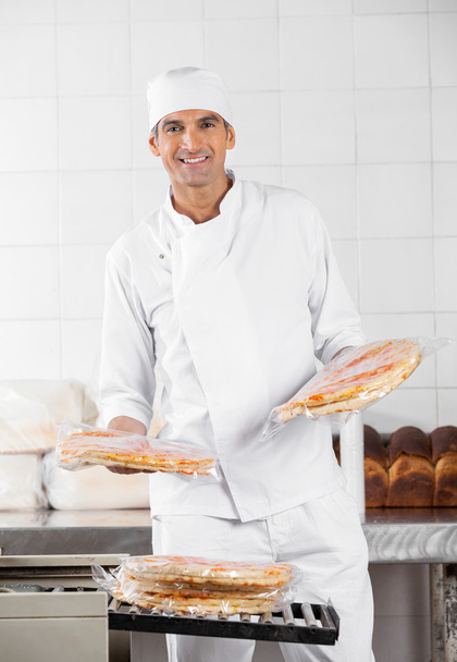 Baker Stacking Packed Pizza Breads In Bakery - Photo, image