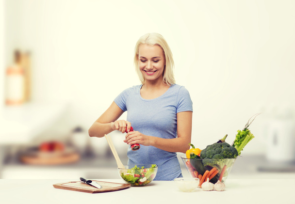 smiling woman cooking vegetable salad on kitchen - Фото, зображення
