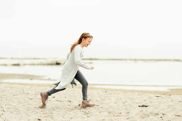 Adorable petite fille de 8-9 ans jouant au bord du lac, portant un pantalon gris et un long cardigan
 - Photo, image
