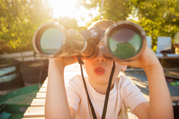 Little boy looking through binoculars on river bank - Fotoğraf, Görsel