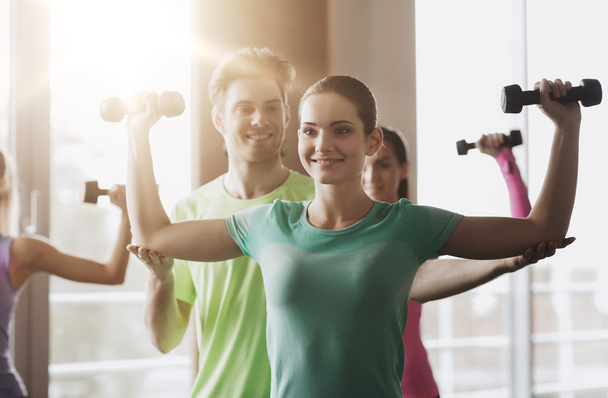 happy women and trainer with dumbbells in gym - 写真・画像