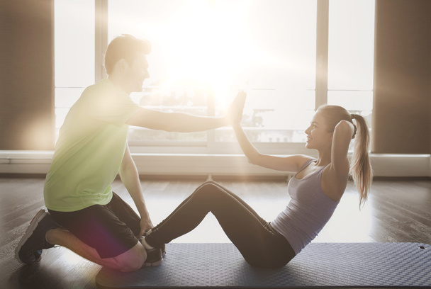 woman with personal trainer doing sit ups in gym - Foto, afbeelding