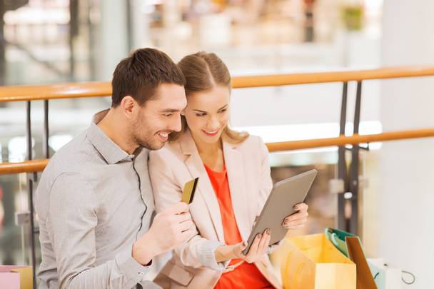 couple with tablet pc and shopping bags in mall - Photo, image