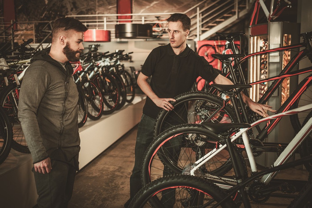 Myyjä esittelee uuden polkupyörän kiinnostuneelle asiakkaalle pyöräkaupassa
. - Valokuva, kuva