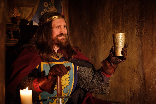 Old medieval king with goblet of wine on the throne in ancient castle interior. - Photo, Image