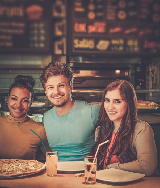 multiraciale vrienden plezier pizza eten in pizzeria. - Foto, afbeelding