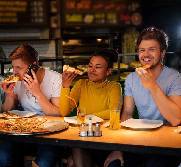 multiracial friends having fun eating pizza in pizzeria. - Photo, Image