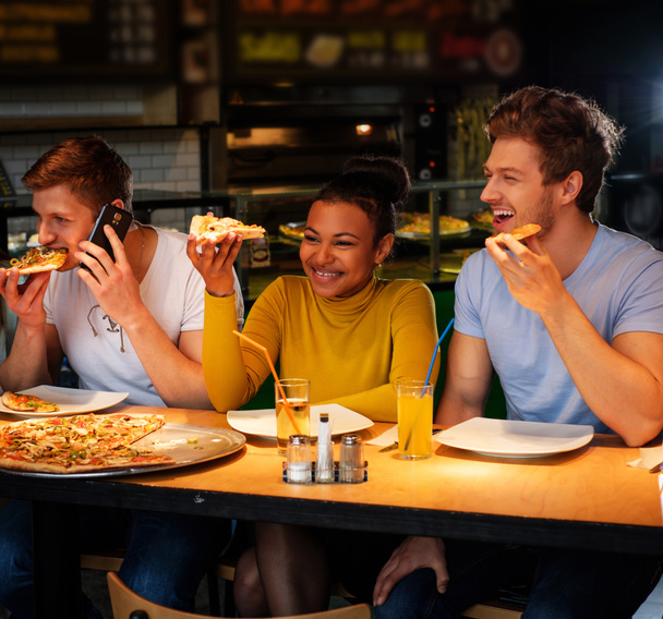 мультирасовые друзья весело едят пиццу в пиццерии
. - Фото, изображение