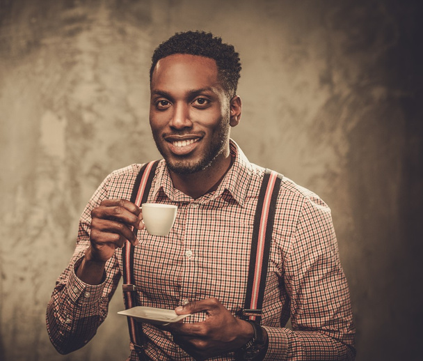 Stylish young black man with cup of coffee posing on dark background.  - Foto, imagen
