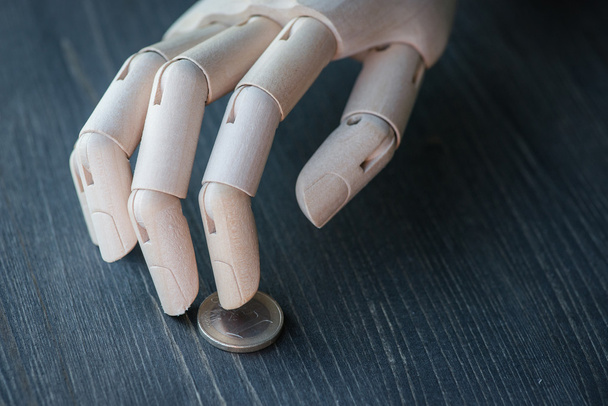 Штучна дерев'яна рука тримає гроші, на дерев'яному столі
 - Фото, зображення
