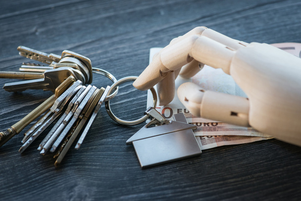 Main artificielle en bois tenant les clés et l'argent, sur une table en bois
 - Photo, image