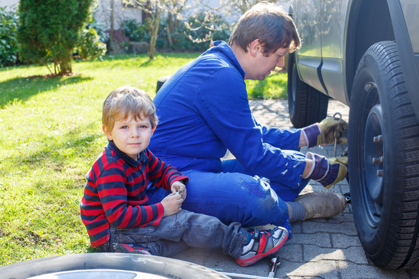 Маленький хлопчик і його батько міняють колесо на машині
 - Фото, зображення
