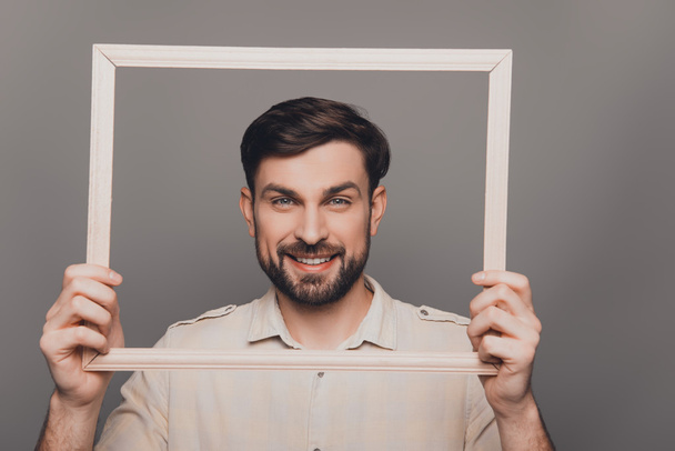 Portrait of happy smiling bearded man  holding wooden frame - Zdjęcie, obraz