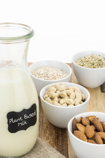 Бутылка самодельного растительного молока и миски с ингредиентами на деревянной поверхности, и белый фон
 - Фото, изображение
