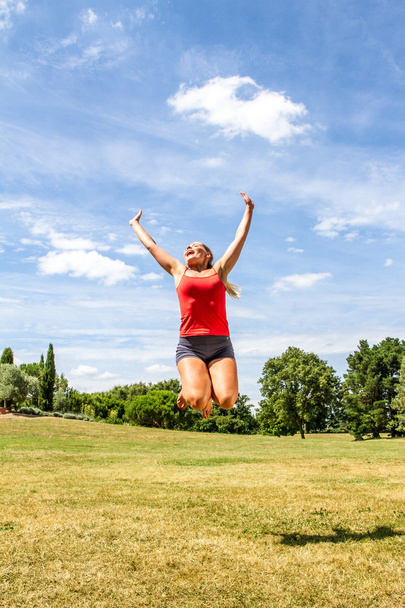 happy young blond woman jumping high to reach the sky to achieve success - Valokuva, kuva