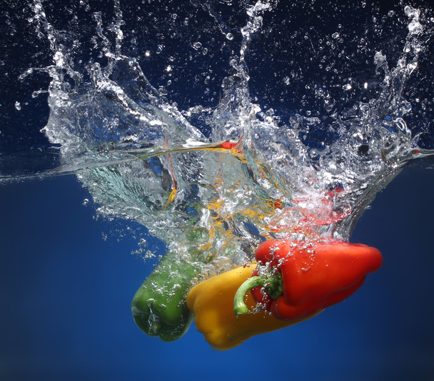 Three peppers falling into water. Blue background - Фото, зображення