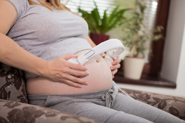Kobieta w ciąży w domu siedzi i odtwarzania muzyki przez headpho - Zdjęcie, obraz
