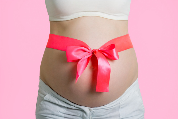 Beautiful young pregnant woman with ribbon. Isolated on pink bac - Photo, image