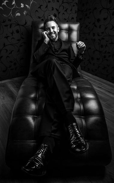 Handsome young man in dark suit relaxing on luxury sofa. Black-white photo. - Φωτογραφία, εικόνα