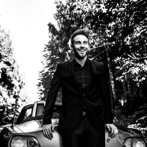 Elegant young fashionable man in convertible car outdoor. Black-white portrait. - Photo, image