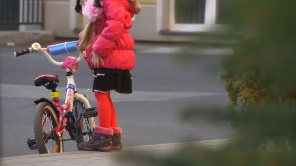 Маленькая девочка поднимает велосипед, едет кататься на велосипеде, пытаясь сидеть на нем Сити-стрит в вечерней асфальтированной дороге ребенок учится ездить на велосипеде
 - Кадры, видео