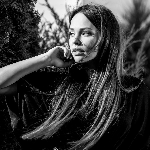 Black-white outdoors portrait of beautiful young girl in luxury long black dress posing in summer garden. - Фото, зображення