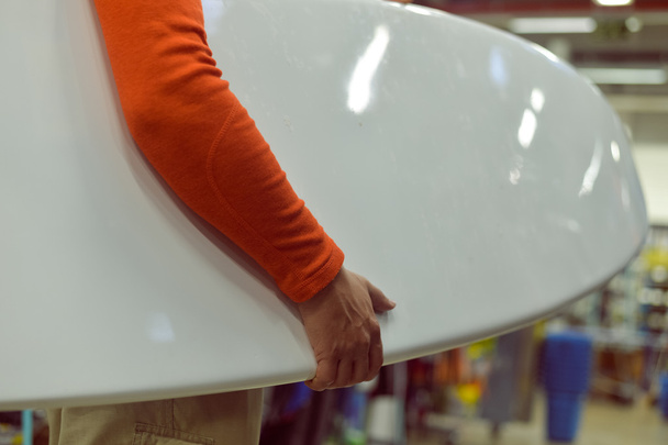 Male surfer holding a surf board on shop background - Fotó, kép