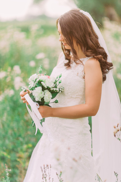 Close-up portrait of beautiful elegant bride in wedding dress holding and looking at luxury natural white bridal bouquet - 写真・画像