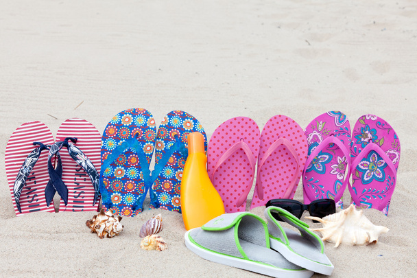 Four pairs bath slippers in a row stuck in the sand beach - Foto, Imagen