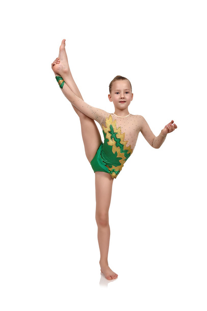 Mała dziewczynka gimnastyczka w zielone ubrania podniósł nogę - Zdjęcie, obraz