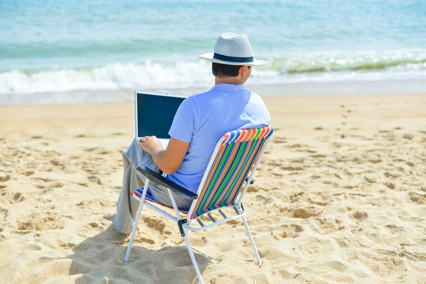 Back side view of relaxed man using laptop, beach background, outside summertime - Foto, Imagen