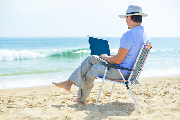 Back side view of relaxed man using laptop, beach background, outside summertime - Фото, изображение