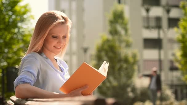 Young beautiful blonde girl in summer day is reading a book  - Filmati, video