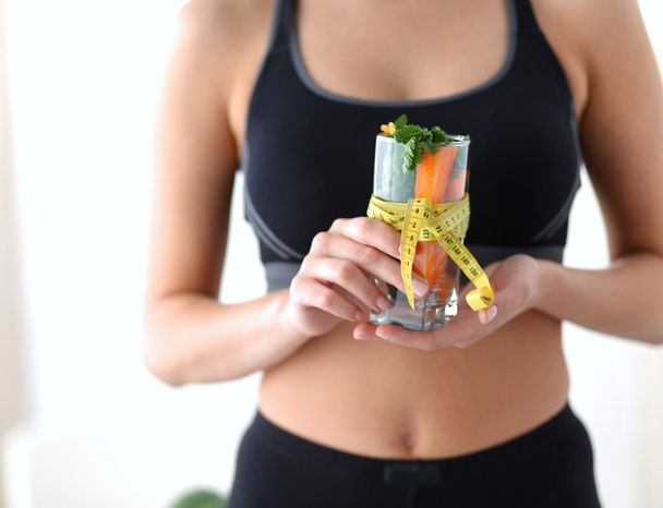 Woman holding a drinking glass full of fresh fruit salad with a tape measure around the glass - Foto, imagen