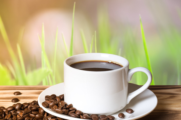 Кофейные зерна и кофе в белой чашке на деревянном столе напротив
  - Фото, изображение