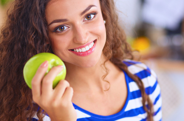 Happy young woman eating apples on kitchen - Fotó, kép