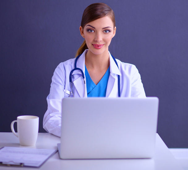Vrouwelijke arts werken zitten op grijze achtergrond - Foto, afbeelding