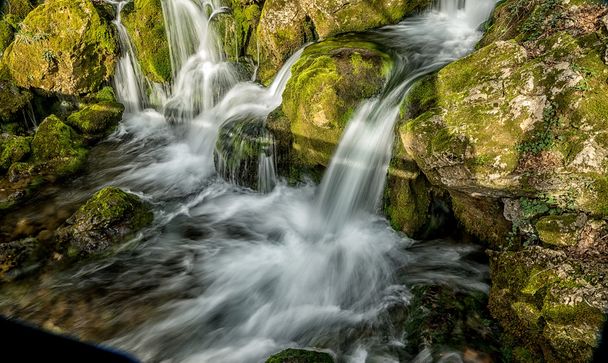 Fuente del río que hace cascadas sobre rocas cubiertas de ingenio
 - Foto, Imagen
