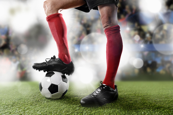 赤い靴下と黒い靴を履いたサッカー選手が、スタジアムのピッチに立つボールを抱えて - 写真・画像