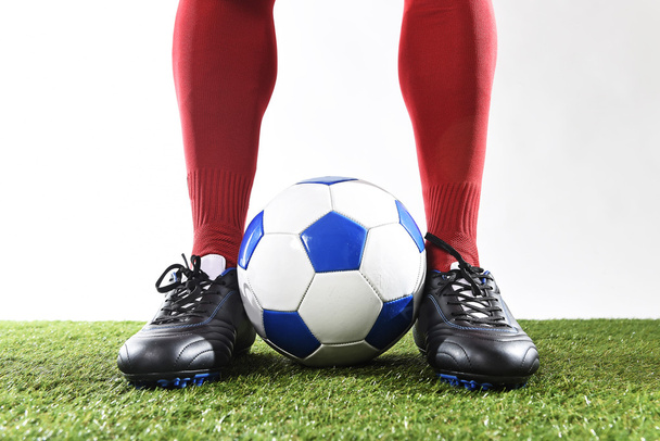 legs feet of football player in red socks and black shoes posing with the ball playing on green grass pitch - 写真・画像