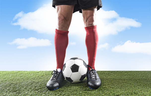 close up legs feet football player in red socks and black shoes playing with ball on grass pitch outdoors - Fotó, kép
