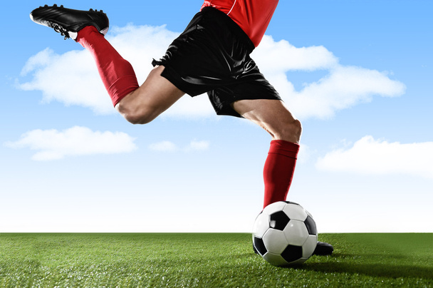 close up legs of football player in red socks and black shoes running and kicking the ball in free kick action playing outdoors - Foto, Imagem