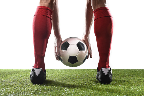 legs of football player in red socks and black shoes holding the ball in his hands placing free kick - Photo, Image