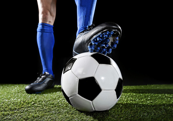 Beine und Füße eines Fußballers in blauen Socken und schwarzen Schuhen posieren mit dem Ball auf grünem Rasen - Foto, Bild